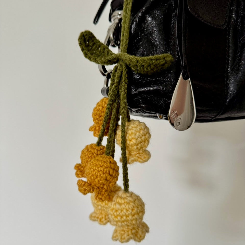 Crocheted yellow and green flower keychain hanging on a bag with neutral background. 