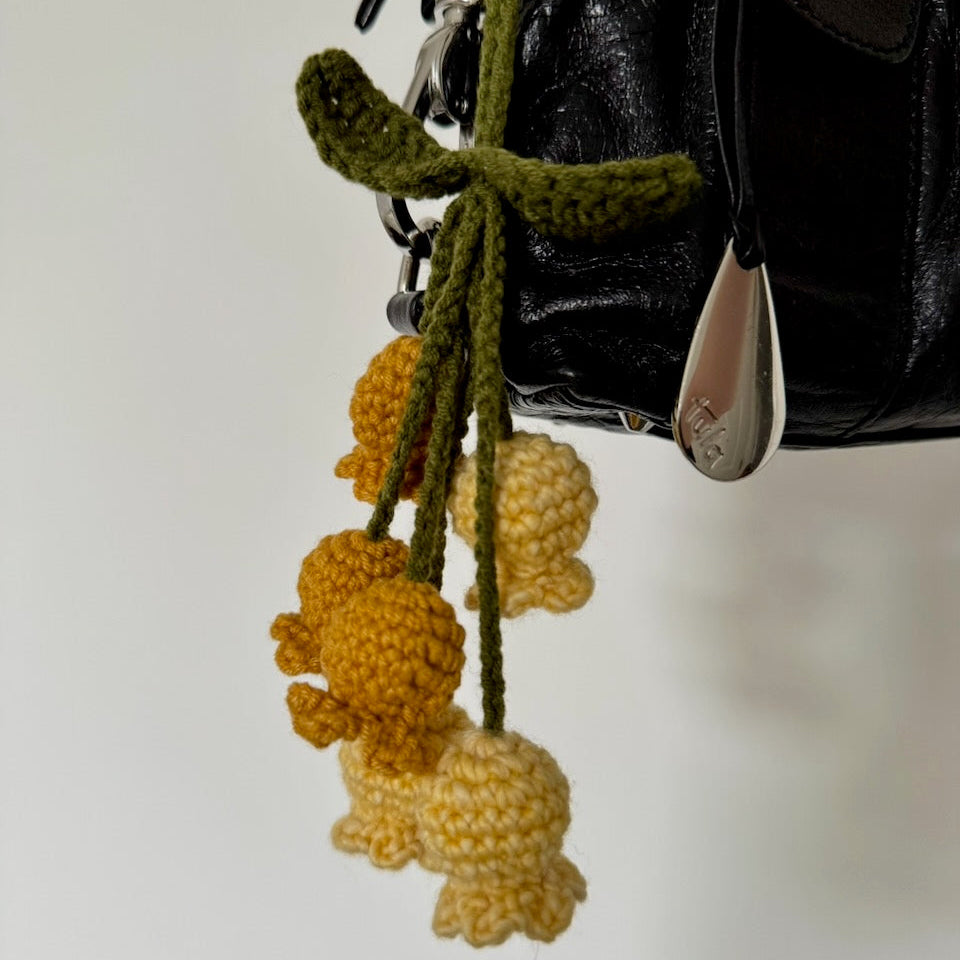 Yellow and green crocheted flower key chain hanging on a bag on a neutral background.
