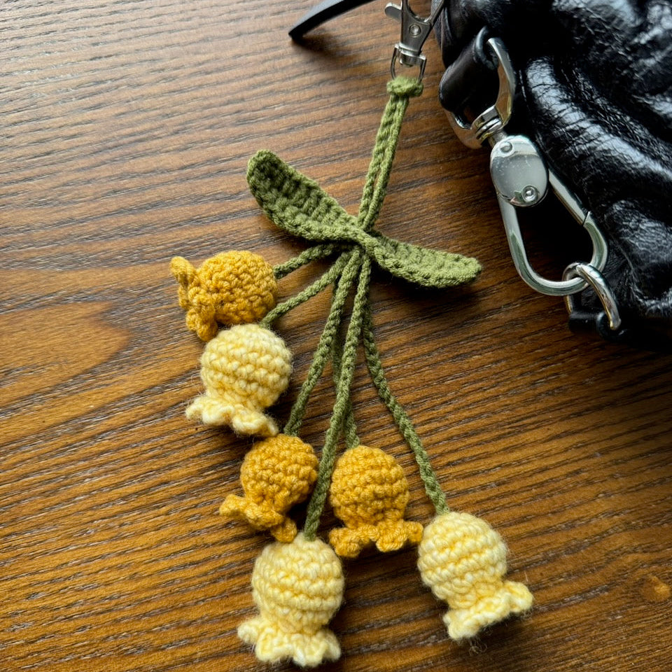 Crocheted yellow and green flower keychain attached to a black bag on a wooden surface